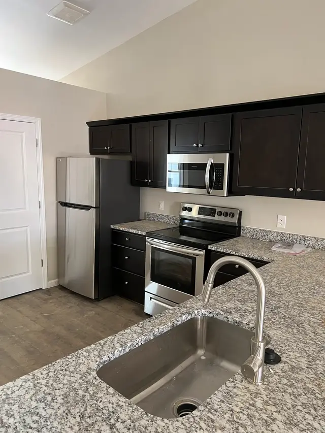 A kitchen seen from the sink, with a range, over-range microwave, refrigerator and granite counters