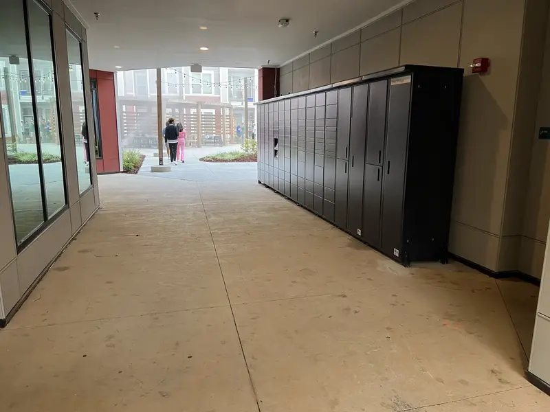 A long bank of dark lockers along a bright covered walkway leading to a courtyard