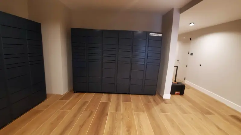 A bank of charcoal parcel lockers in a clean indoor lobby with a wood-look floor