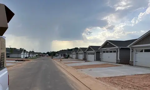 A new-construction street of identical townhomes under a stormy sky, with bare graded dirt and fresh concrete