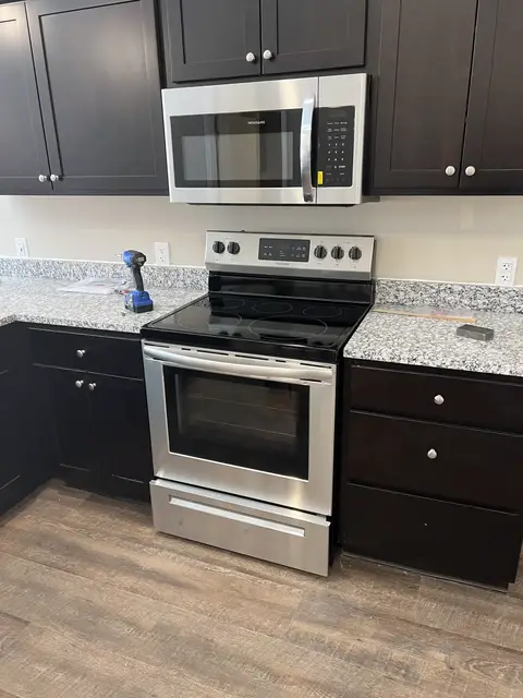A new range and over-range microwave just set between dark cabinets, with a cordless drill and a manual on the counter