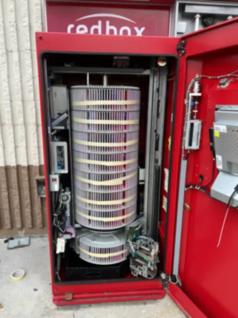 A kiosk with its door open, showing the disc carousel, power conditioner and computer inside